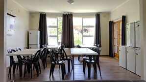 Una habitación con una mesa de comedor y sillas, un refrigerador y una ventana con cortinas.