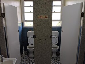 Un baño público con dos inodoros, un lavamanos y un cartel de 'No Smoking'.