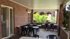 Un área de patio al aire libre con paredes de ladrillo, mesas blancas y sillas negras.
