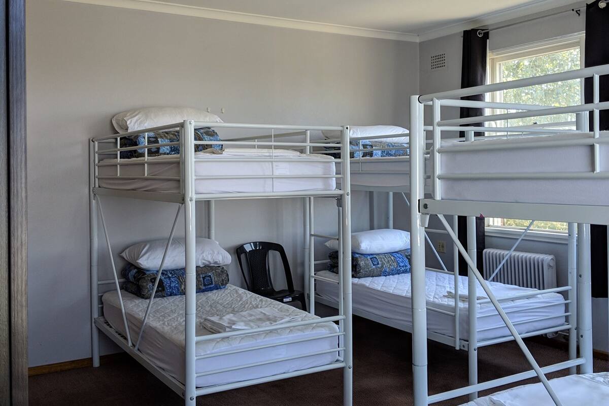 Una habitación con literas, ventilador de techo, ventana con cortinas y radiador.