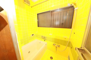 A bathroom with yellow tiles, a bathtub, a shower, and a window.