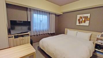 A hotel room with a bed, a TV on a stand, a bedside table, a window with curtains, and a wall-mounted artwork.