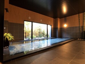 A modern indoor swimming pool with a view of trees and a bamboo fence outside. - Hotel Route Inn Yamanashi Chuo (Chuo)