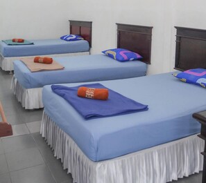 Ein Hotelzimmer mit drei Betten, jedes mit blauer Bettdecke und weißem Bettschurz.