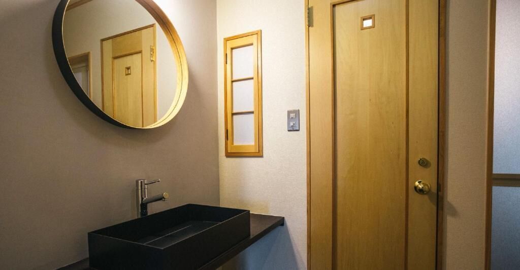A bathroom with a rectangular sink, a round mirror, and a wooden door.