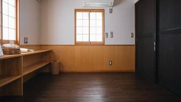 A room with a wooden floor, a window with a view, a shelf with items, and a door.
