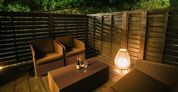 Un patio al aire libre con mobiliario de mimbre, una mesa con botellas y vasos, y una lámpara.