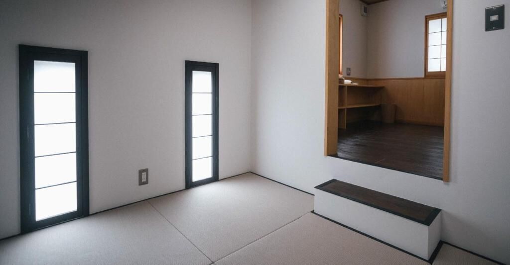 Una habitación con suelo de esteras de tatami, un banco de madera bajo y una puerta corredera.