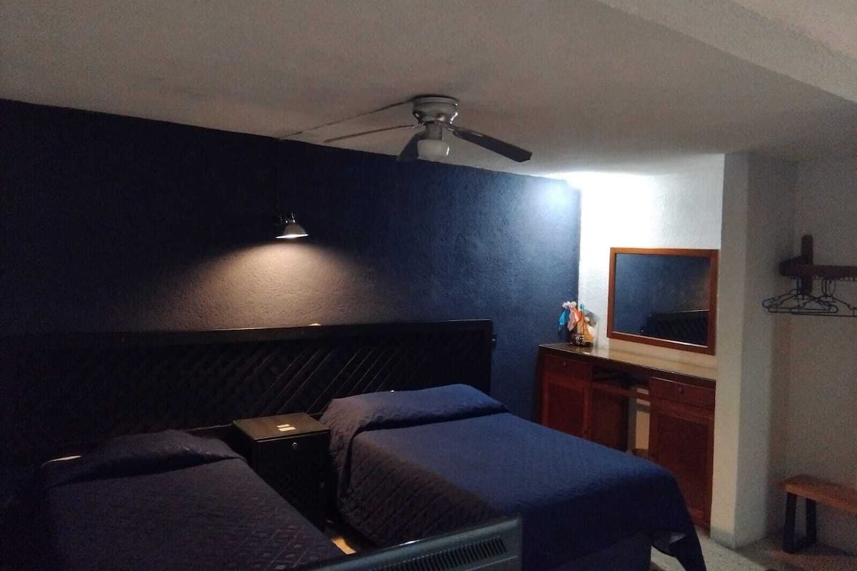 A bedroom with a bed, a desk, a mirror, and a ceiling fan.