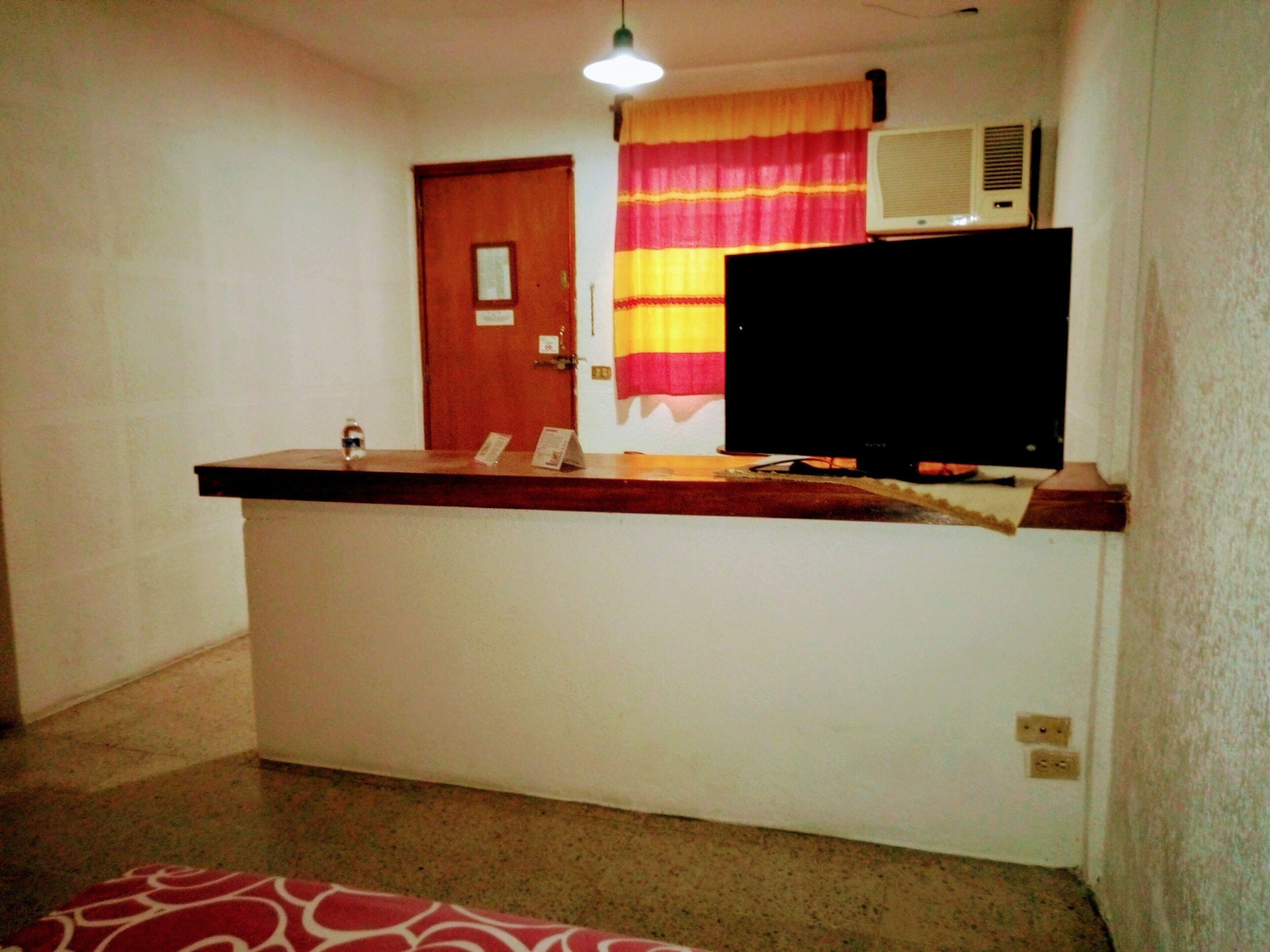A reception desk with a flat-screen TV, a wooden counter, and a door in the background.