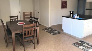 A dining area with a wooden table and chairs, a kitchen with white cabinets and a black countertop, and a ceiling fan. - Rustic Cottage Feel, Close to Wineries, Sleeps 6! (Cornville)