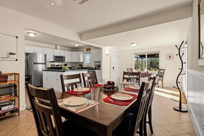 A modern kitchen with white cabinets, stainless steel appliances, and a dining area with a wooden table set for four. - Rustic Cottage Feel, Close to Wineries, Sleeps 6! (Cornville)