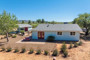 A single-story house with a red door, a small patio with a table and chairs, and a clear view of the surrounding landscape. - Rustic Cottage Feel, Close to Wineries, Sleeps 6! (Cornville)