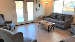 A living room with a sofa, chairs, a coffee table, and a lamp. There are framed pictures on the wall and a door leading outside. - Rustic Cottage Feel, Close to Wineries, Sleeps 6! (Cornville)