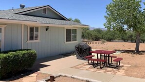 A single-story house with a covered patio area, a barbecue grill, and a tree in the background. - Rustic Cottage Feel, Close to Wineries, Sleeps 6! (Cornville)