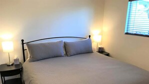 A neatly made bed with a headboard, two bedside tables with lamps, and a window with blinds. - Rustic Cottage Feel, Close to Wineries, Sleeps 6! (Cornville)