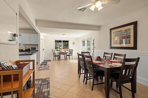 A dining area with a wooden table and chairs, a kitchen in the background, and a framed painting on the wall. - Rustic Cottage Feel, Close to Wineries, Sleeps 6! (Cornville)