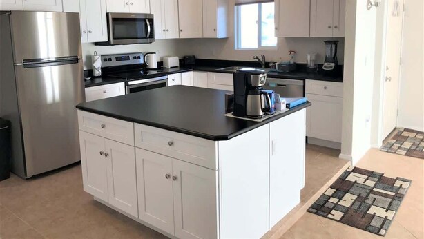 A modern kitchen with white cabinets, a stainless steel refrigerator, a microwave, and a coffee maker. - Rustic Cottage Feel, Close to Wineries, Sleeps 6! (Cornville)