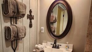 A bathroom with wooden panel walls, a round mirror, a sink with a soap dispenser, and towels hanging on a rack. - The BirdDog Farm Cabin #4    (Dixon Springs)