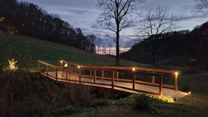 A wooden bridge with railings and lights, surrounded by grass and trees. - The BirdDog Farm Cabin #4    (Dixon Springs)