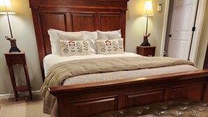 A large wooden bed with a matching bench, two bedside tables with lamps, and a door in the background. - The BirdDog Farm Cabin #4    (Dixon Springs)