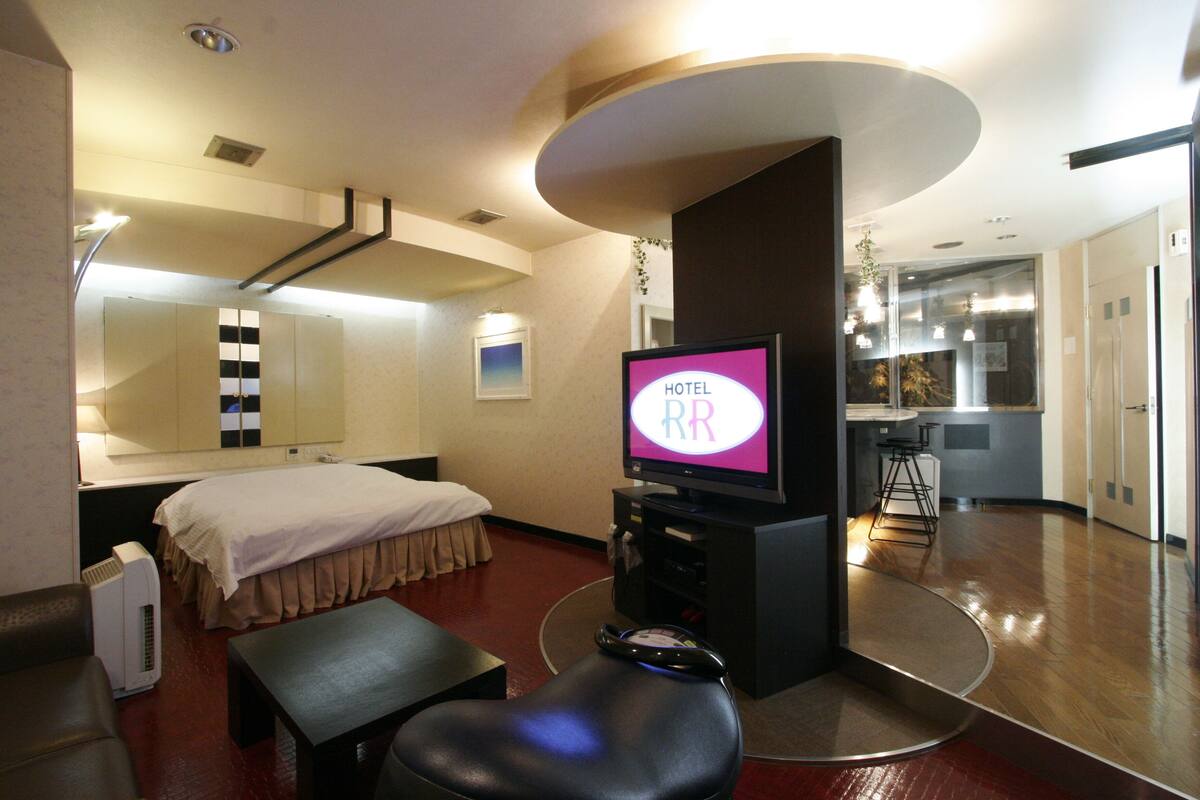 A hotel room with a bed, a desk, a television, and a kitchenette.