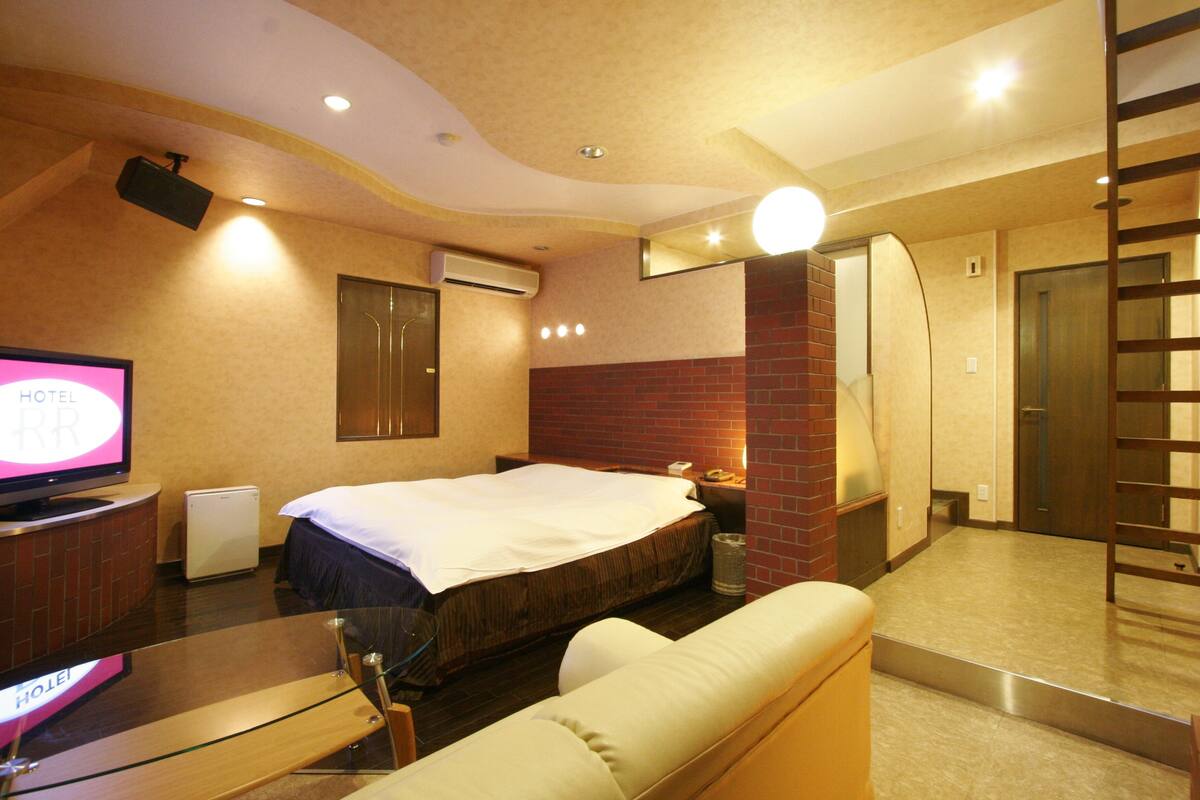 A hotel room with a bed, a television, a desk, a chair, a sofa, and a mirror.