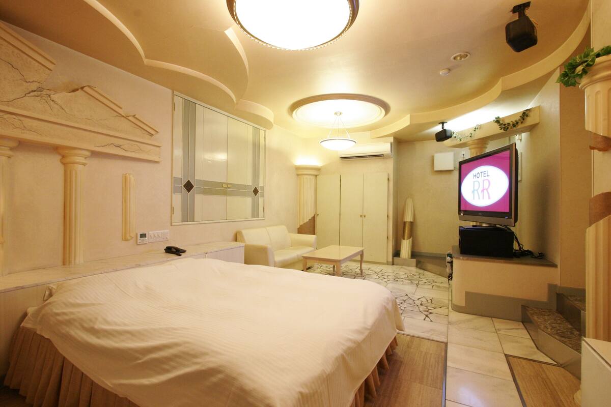 A hotel room with a large bed, a small sofa, a TV, and a mirror.