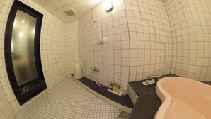 Ein Badezimmer mit weißen Fliesen, einem spiegel mit schwarzem Rahmen, einer Duschkabine mit Handbrause, einem Waschbecken mit Seifenspender und einer Badewanne in Rosa.