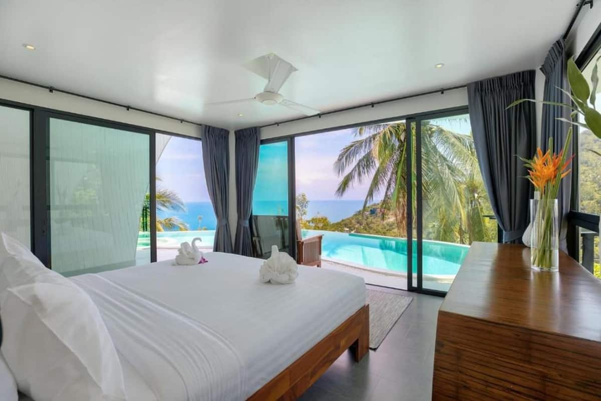 Quarto de hotel moderno com uma cama grande, uma escrivaninha de madeira e vista para uma piscina e oceano.