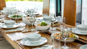 Una mesa de comedor dispuesta con platos, cuencos y vasos blancos, sobre individuales tejidos.