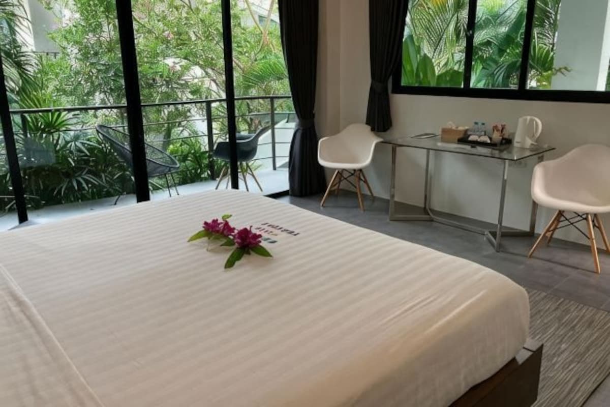 A hotel room with a bed, a small table, two chairs, and a balcony with plants.