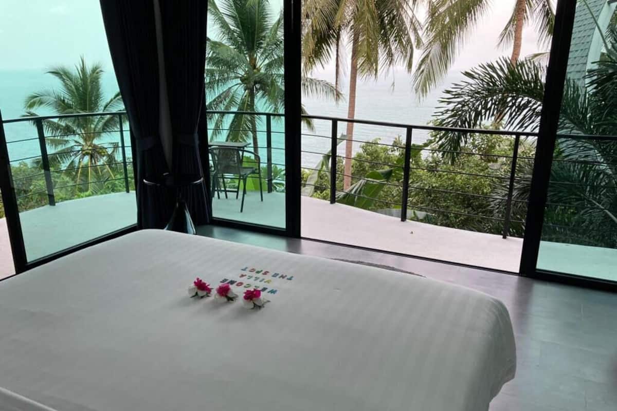 Quarto de hotel com uma cama grande, vista para o oceano e varanda com palmeiras.