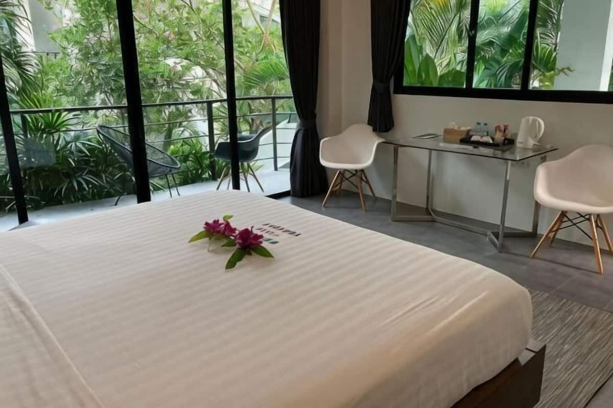 Quarto de hotel com cama, uma mesa pequena, duas cadeiras e varanda com plantas.