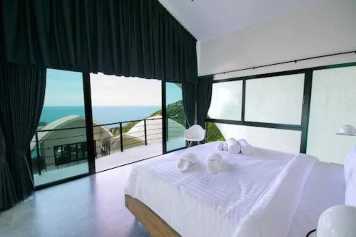 Quarto de hotel moderno com uma cama grande, toalhas brancas e uma varanda com vista para o mar.