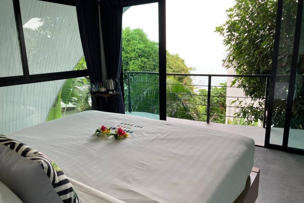 Quarto com uma cama grande, vista para o verde e uma varanda com grade.
