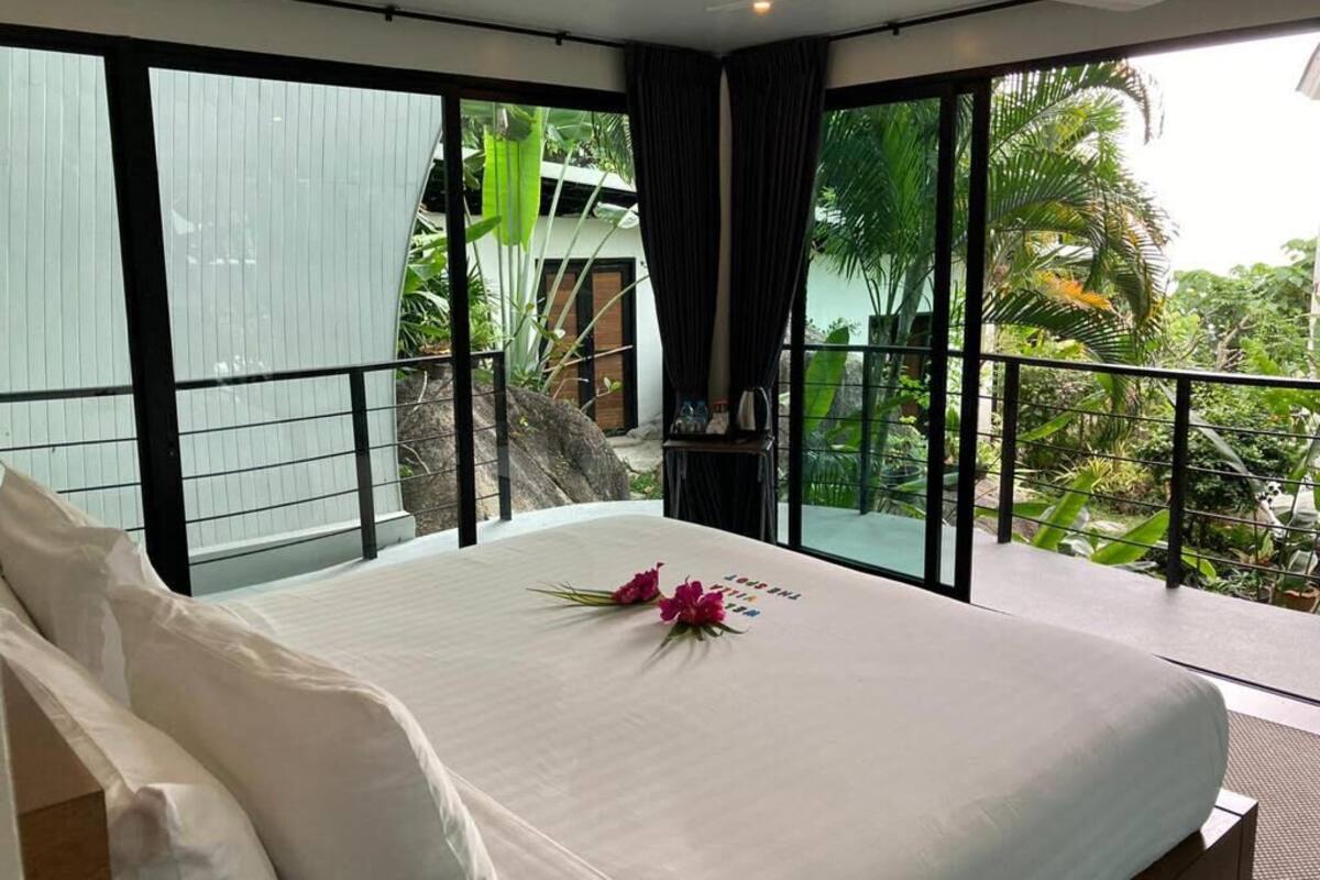 Quarto com uma cama grande, varanda com vista para vegetação e janela com cortinas.