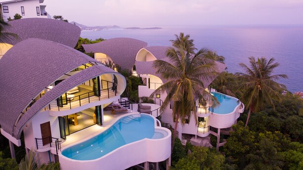 Un resort moderno con varias piscinas, una piscina central amplia y vistas al mar.