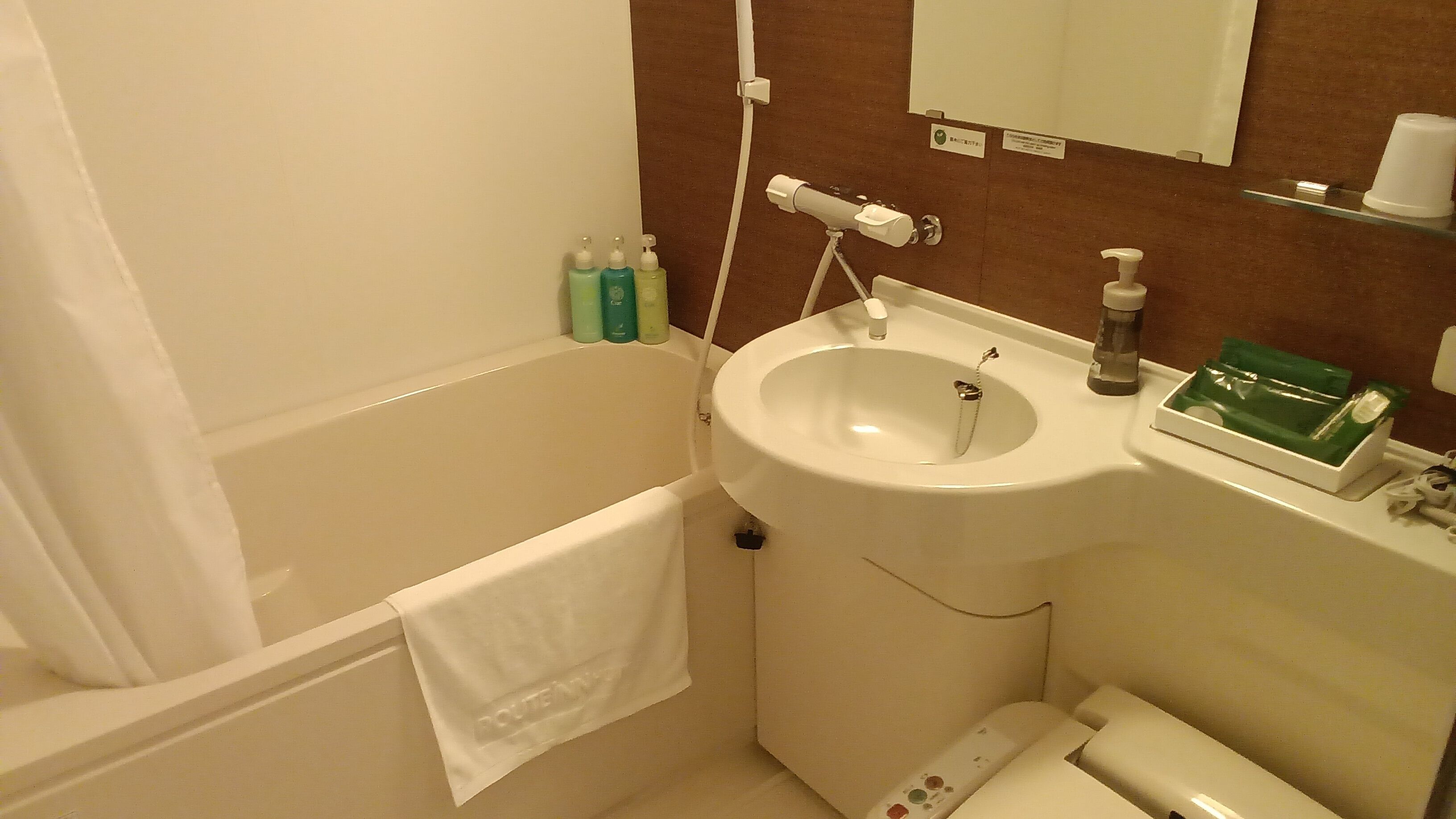 A bathroom with a bathtub, a sink, and a toilet. There are toiletries on the sink and a towel hanging on the wall.