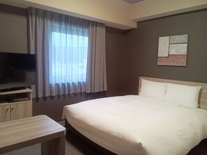 A hotel room with a bed, a TV on a stand, a small table, and a window with curtains. - Hotel Route Inn Hamada Ekimae (Hamada)