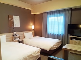 Una habitación de hotel con dos camas, un escritorio, una televisión, una lámpara y una ventana con cortinas.
