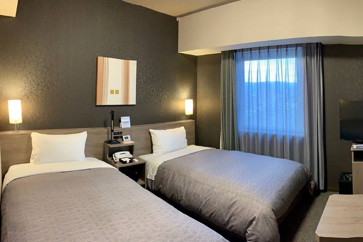 A hotel room with two beds, a bedside table with a phone, a lamp, and a painting on the wall.