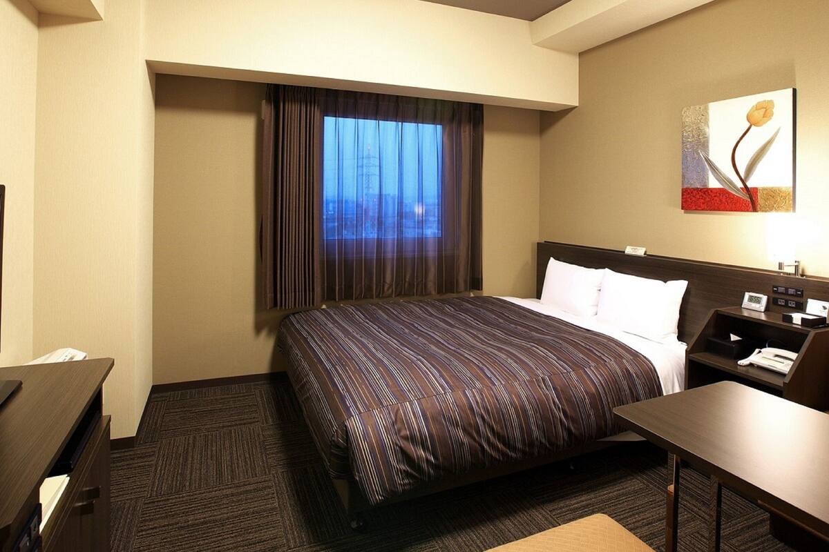 A hotel room with a large bed, a desk, a chair, a nightstand, and a painting on the wall.