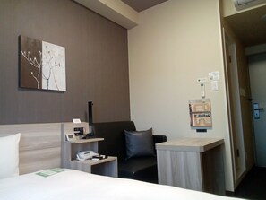 A hotel room with a bed, a desk, a chair, a wall-mounted phone, and a painting. - Hotel Route Inn Hamada Ekimae (Hamada)