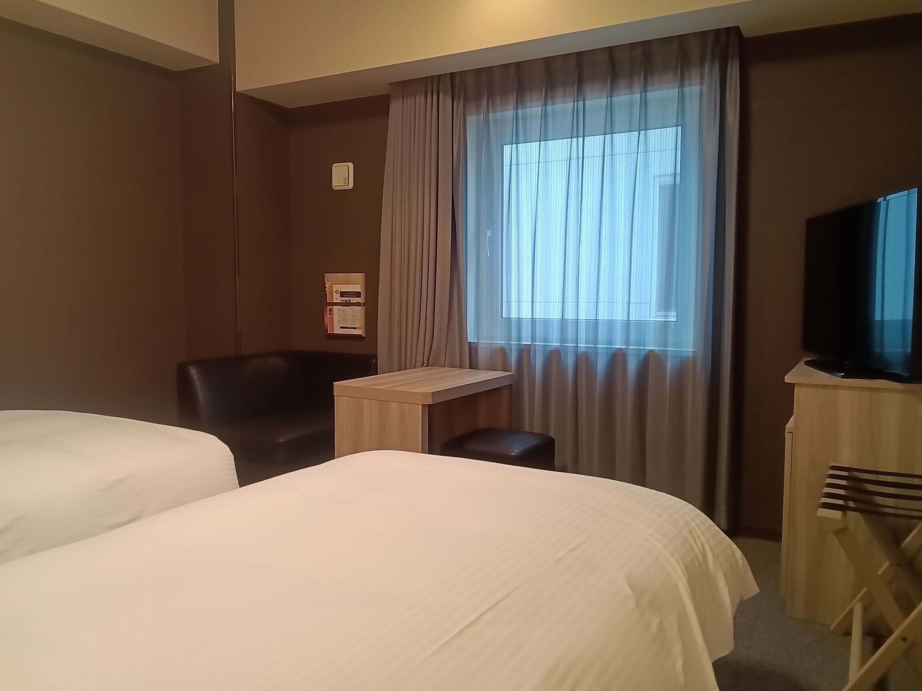A hotel room with two beds, a desk, a chair, a television, and a window with curtains.