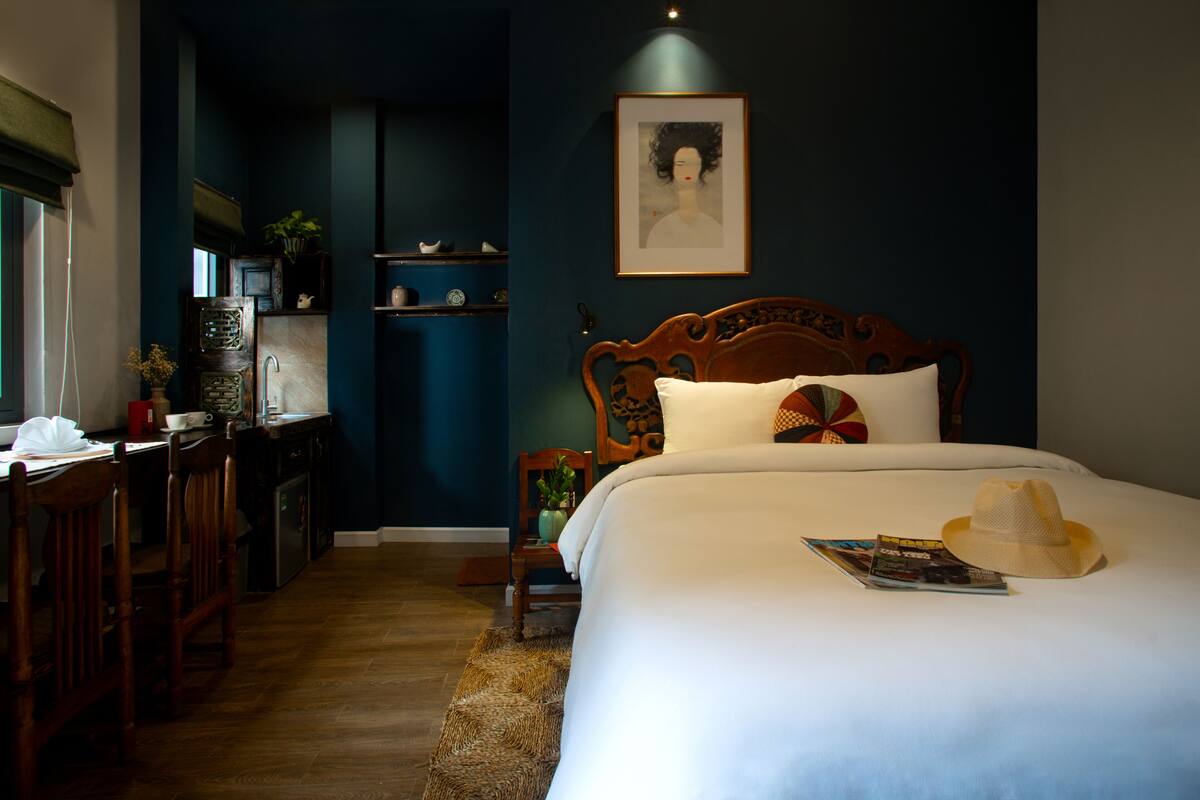 A bedroom with a wooden bed, a bedside table, a chair, a desk, and a shelf with decorative items.