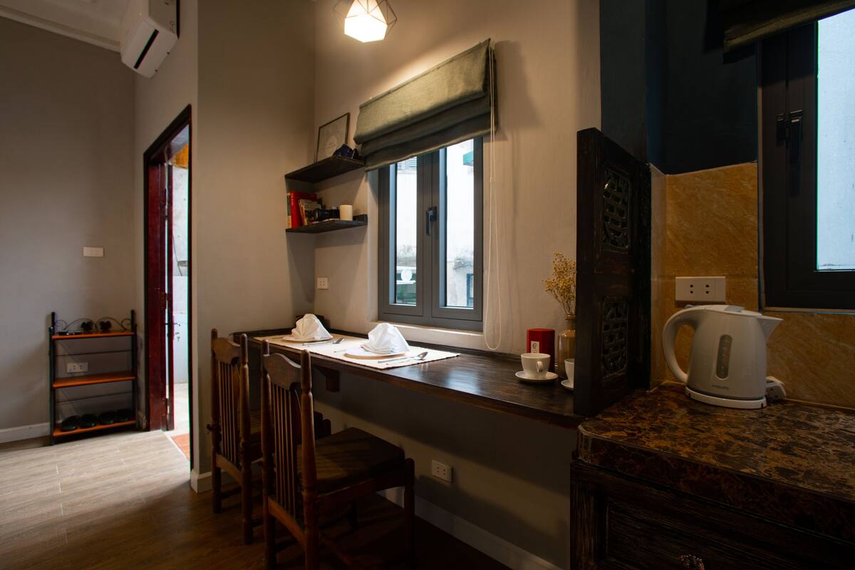 A kitchen with a wooden countertop, a window with blinds, a kettle, and a chair.