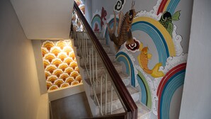 A staircase with a handrail, a wall with colorful fish and cloud patterns, and a patterned wall on the left. - Centraltique Hidden Oasis (Hanoi)