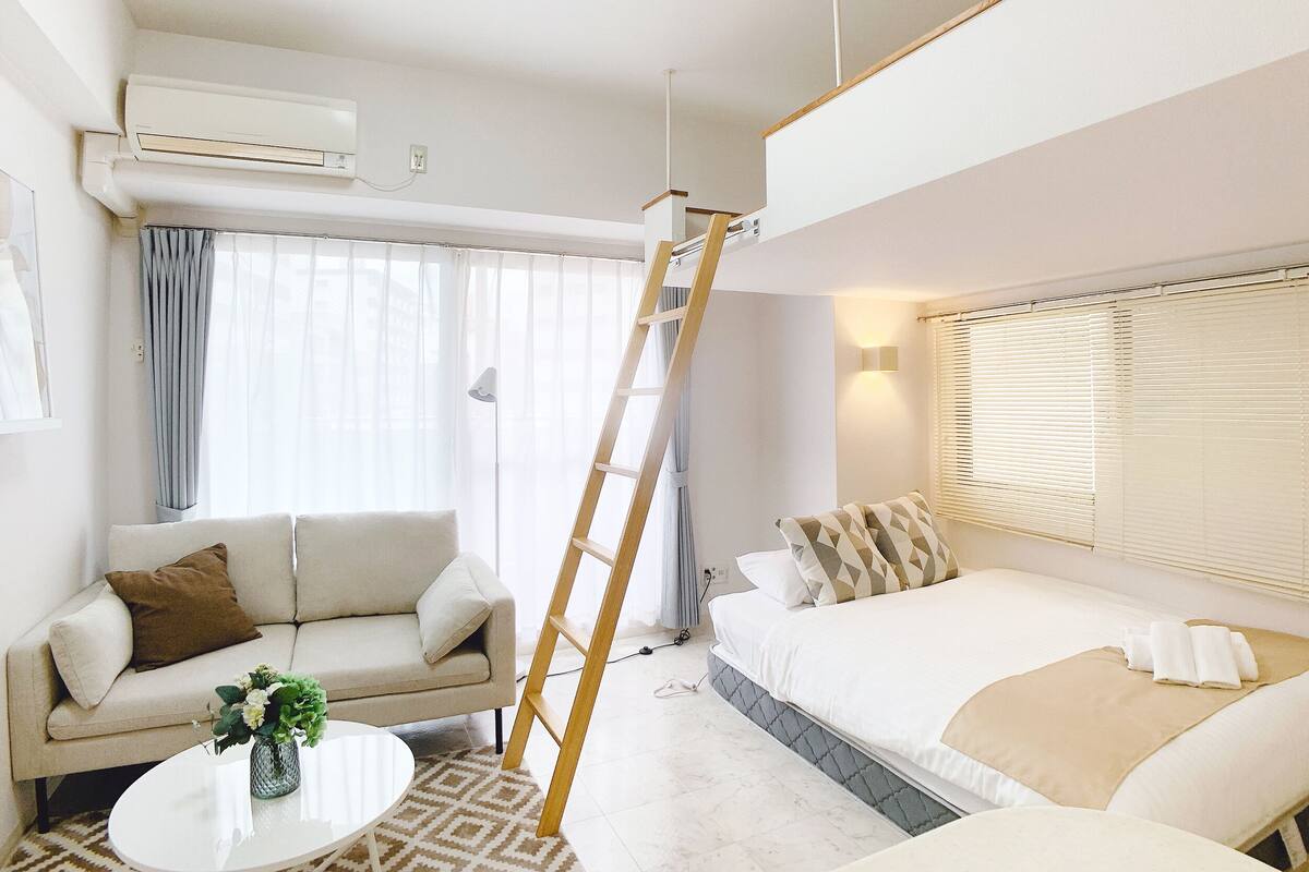 A modern hotel room with a sofa, a bed, a ladder, and a table with a vase.