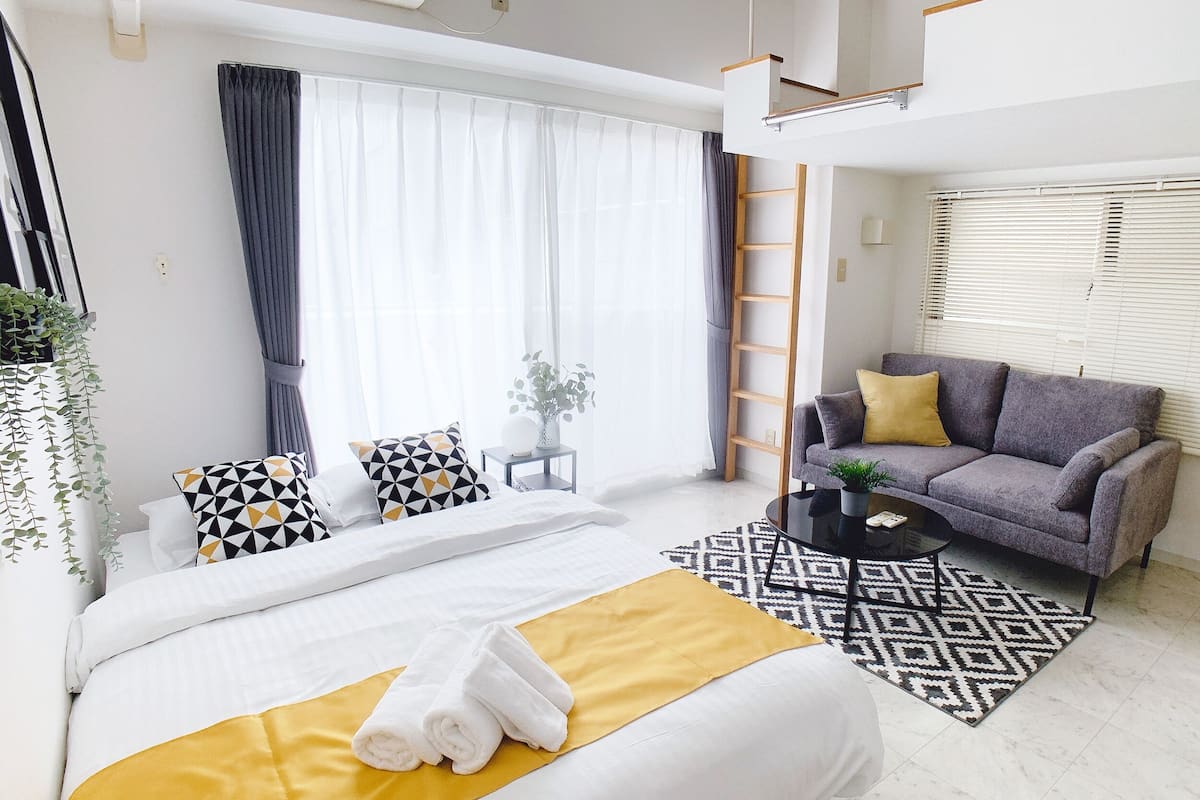 A modern hotel room with a large bed, a sofa, a coffee table, and a view of the outdoors.